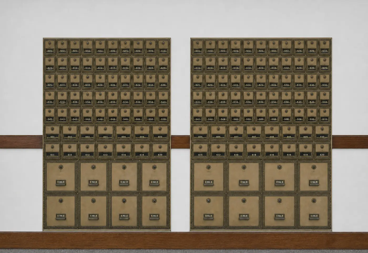 Two tall banks of antique brass post office boxes fill a pale wall, seen straight on in flat, even light. Rows of small doors with round dials and numbered plates run across the top two thirds; four large doors fill each of the bottom two rows. A dark wooden rail crosses the wall behind the banks, and a wooden board runs along the floor.